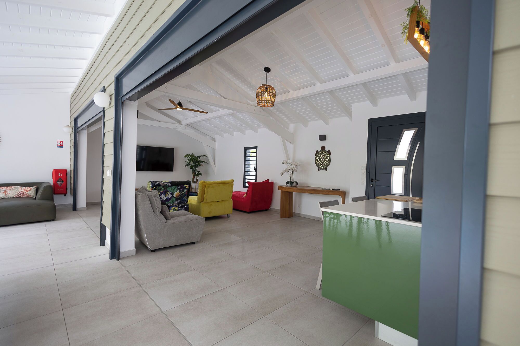 A spacious living area with a high ceiling, a flat-screen TV, a dining table, and a green accent wall.
