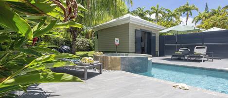 A swimming pool with lounge chairs, a small building, and surrounding greenery.