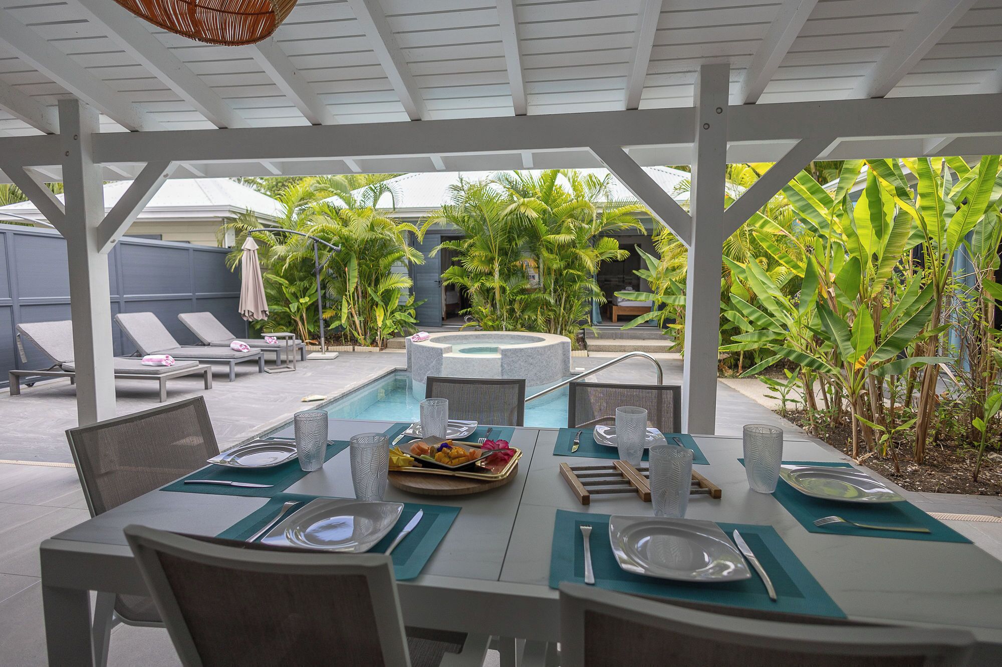 An outdoor dining area with a pool, lounge chairs, and tropical plants.