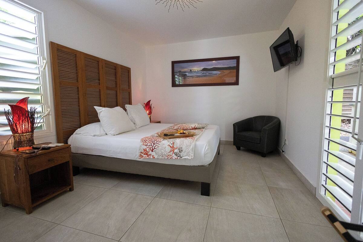 Ein Schlafzimmer mit Bett, Nachttisch, Sessel, Fernseher und einem Bild an der Wand.