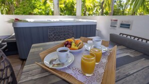 A breakfast tray with coffee, juice, and fruit on a table with a view of a hot tub and greenery. - Majesty Palm (Saint-François)