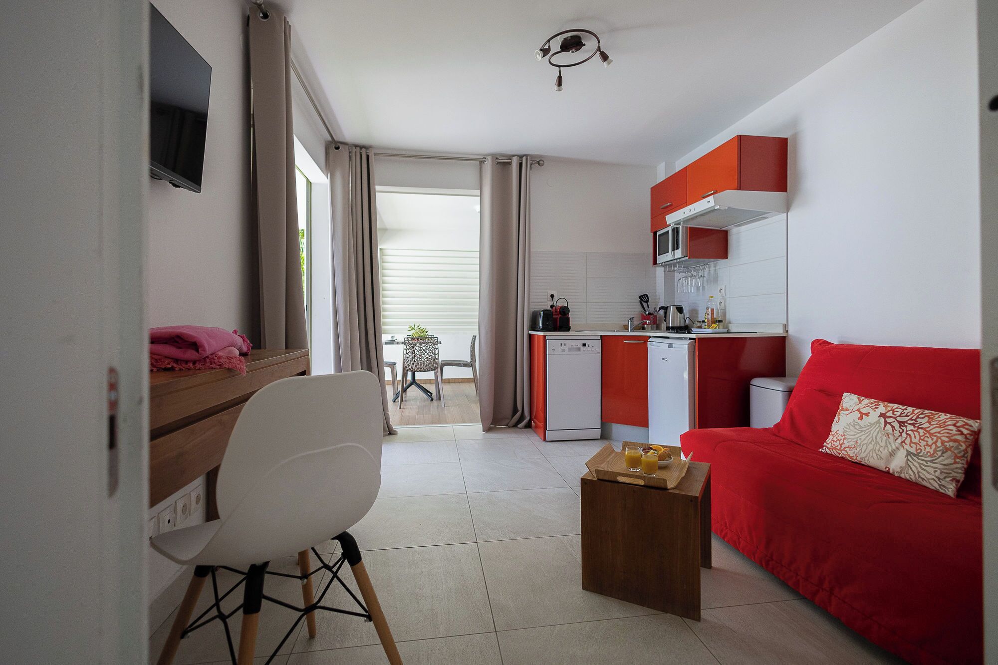 Ein kompakter Wohnraum mit Küchenzeile, Essbereich und einem roten Sofa.