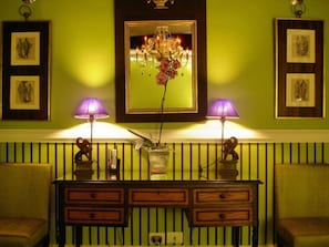 Une pièce avec un mur vert, un miroir orné d’un lustre, deux lampes et une console en bois dotée de tiroirs.