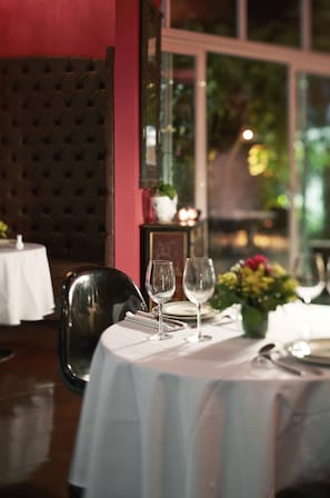 Une table à manger dressée avec des nappes blanches, des verres à vin et un vase rempli de fleurs.