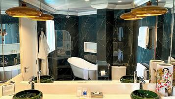 Un baño moderno con un espejo grande, dos lámparas colgantes, una bañera independiente y un lavabo con un grifo de color verde.