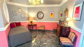 Une chambre d’hôtel avec un lit, deux chaises, un bureau, une lampe, un lustre et des œuvres d’art accrochées aux murs.