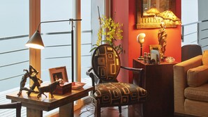 Un salón amplio con ventanas grandes, una mesa de centro de madera, un sillón estampado y un sofá.