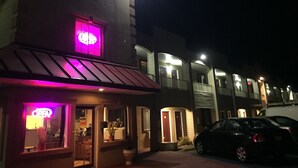 A motel with a neon sign, a car parked in front, and a well-lit entrance.