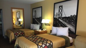 A hotel room with two beds, a desk, a chair, a mirror, and a cityscape painting on the wall.