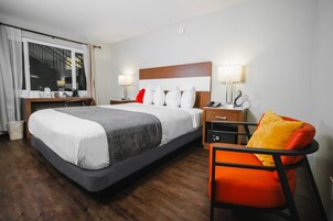 A hotel room with a large bed, bedside tables, a chair, and a window with curtains.