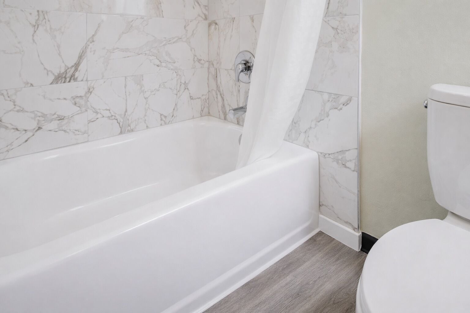 Un baño con una bañera blanca, un inodoro y paredes con diseño de mármol.
