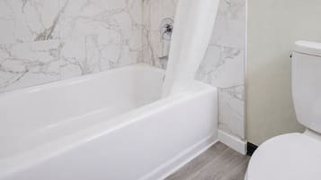 Un baño con una bañera blanca, un inodoro y paredes con diseño de mármol.
