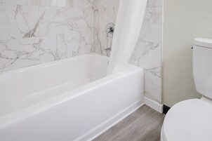 Un baño con una bañera blanca, un inodoro y paredes con diseño de mármol.