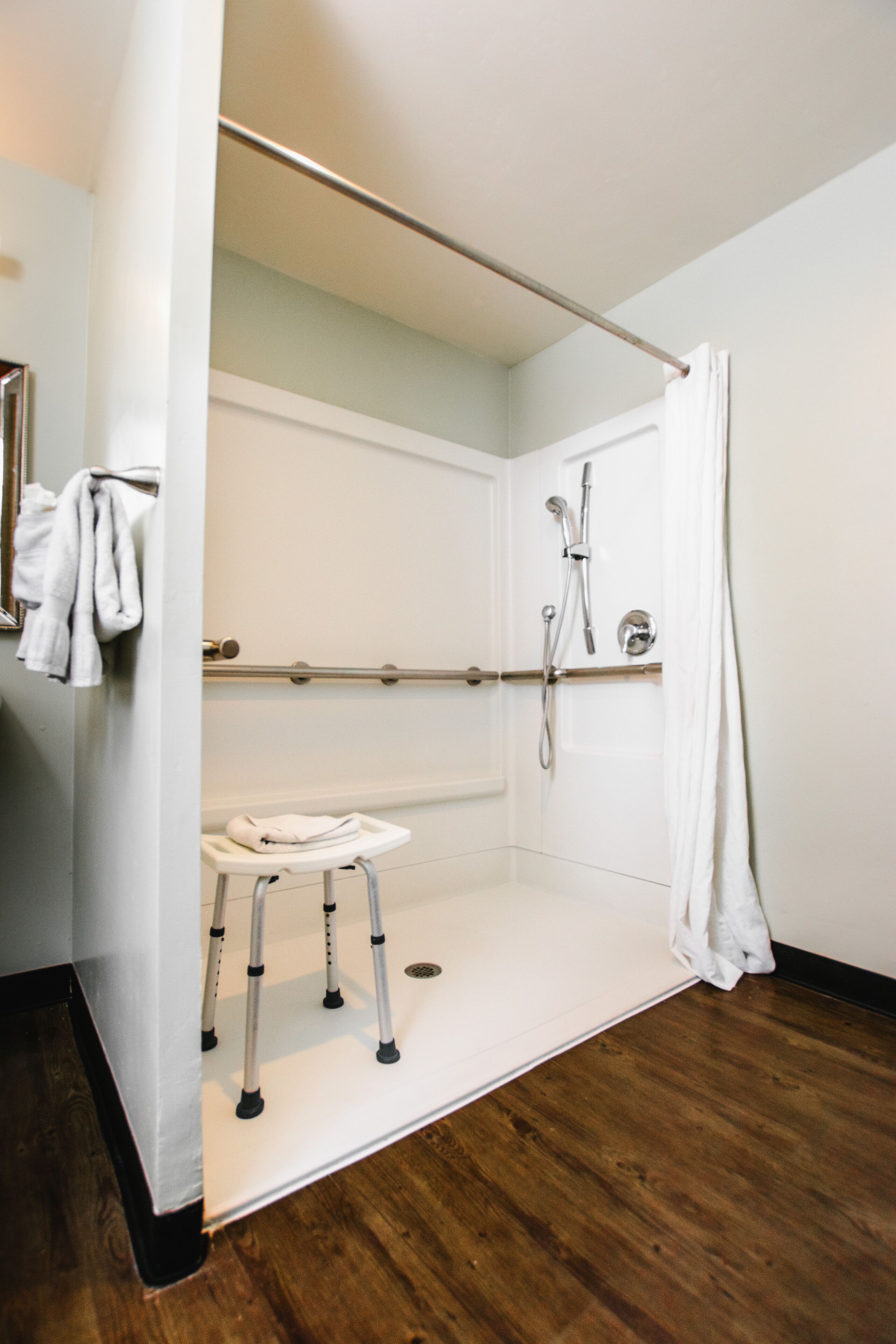 A wheelchair-accessible shower with a grab bar, a white sink, and a wooden floor.