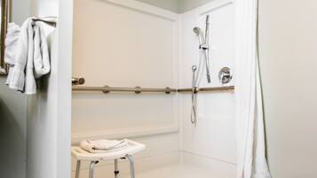 A wheelchair-accessible shower with a grab bar, a white sink, and a wooden floor.