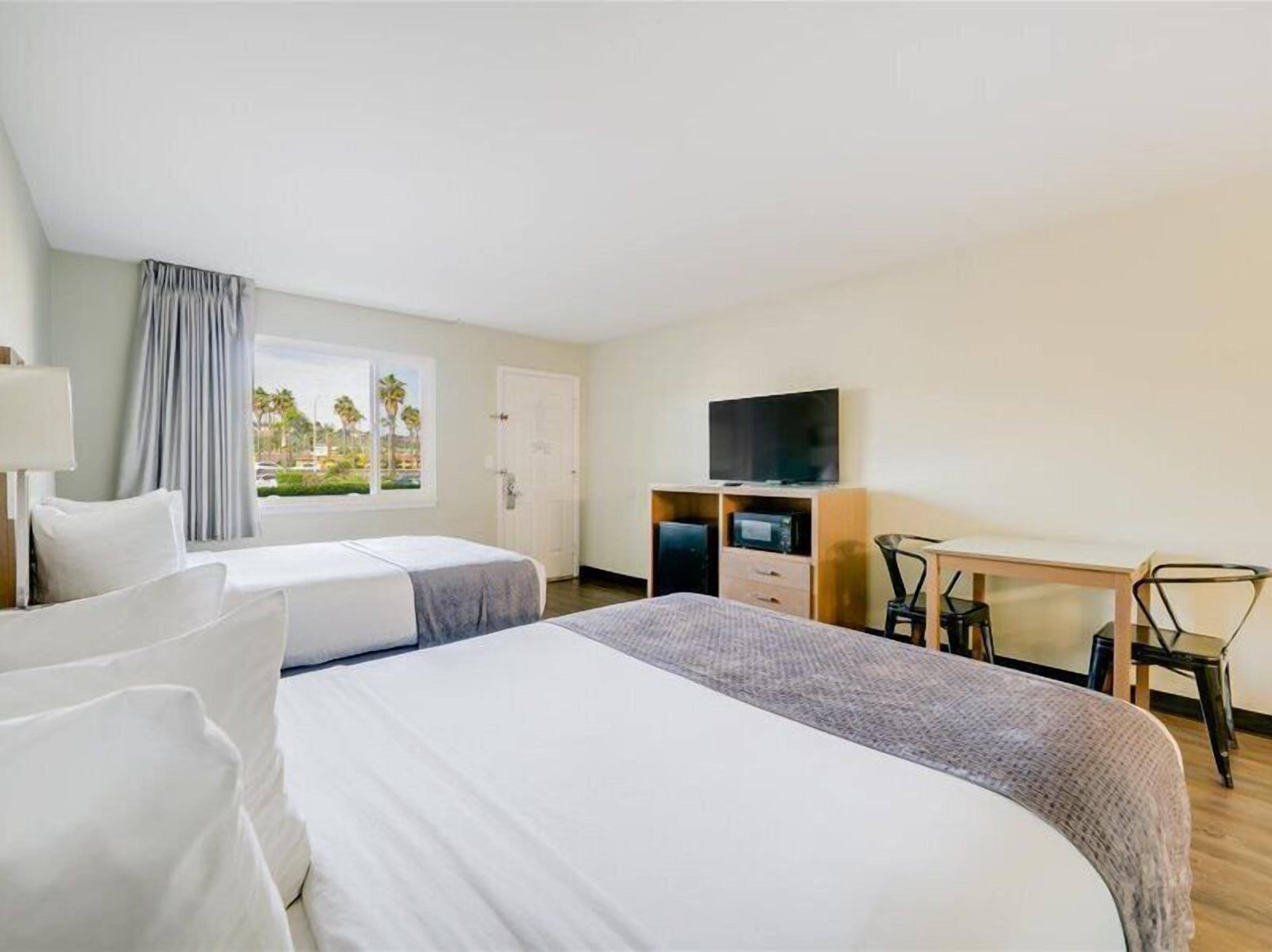 A hotel room with two beds, a desk with a chair, a television, and a window with curtains.