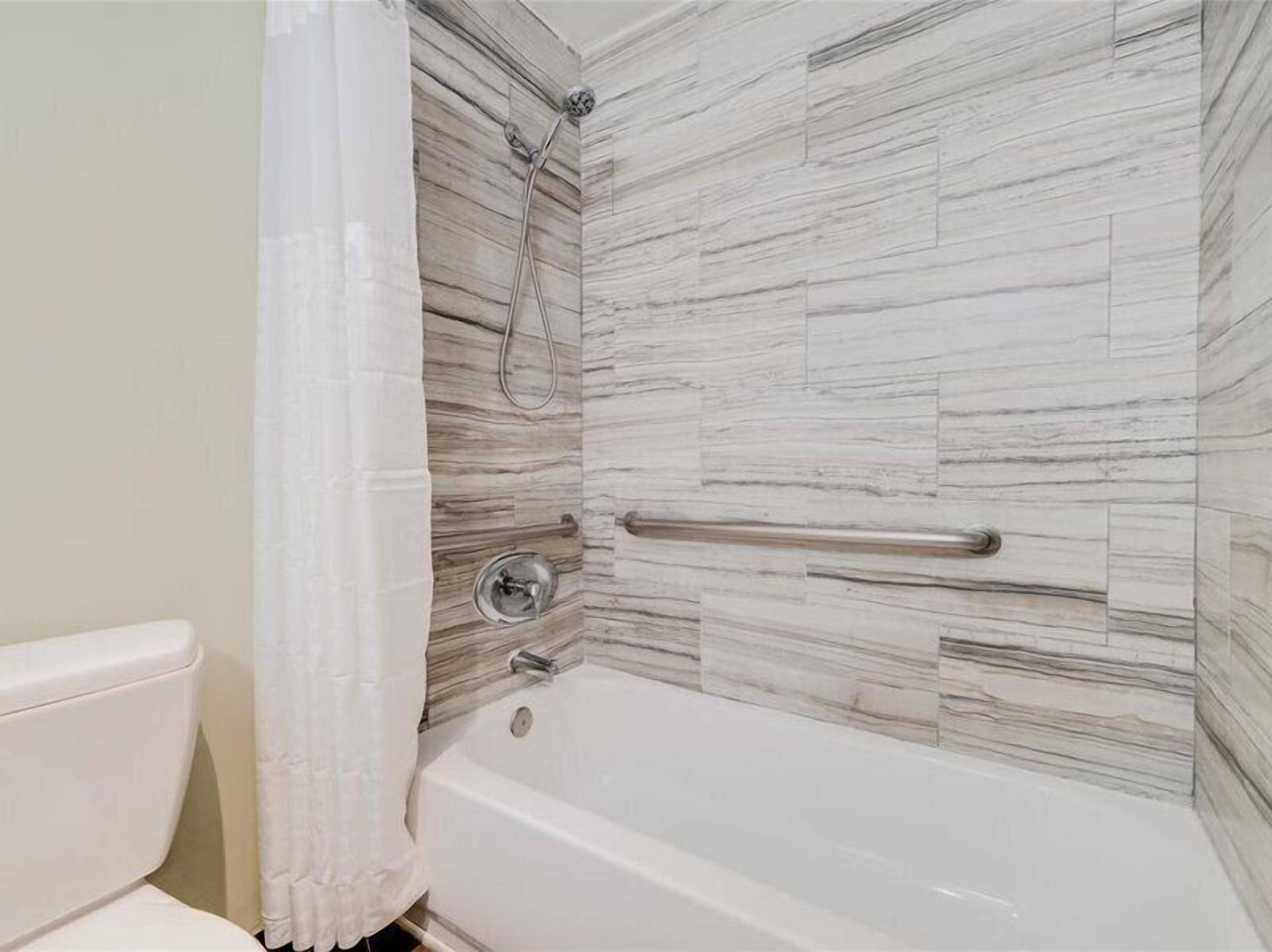 A bathroom with a white bathtub, a shower with a handheld showerhead, and a toilet.