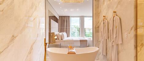 A modern bathroom with a freestanding bathtub, marble walls, and a large chandelier.