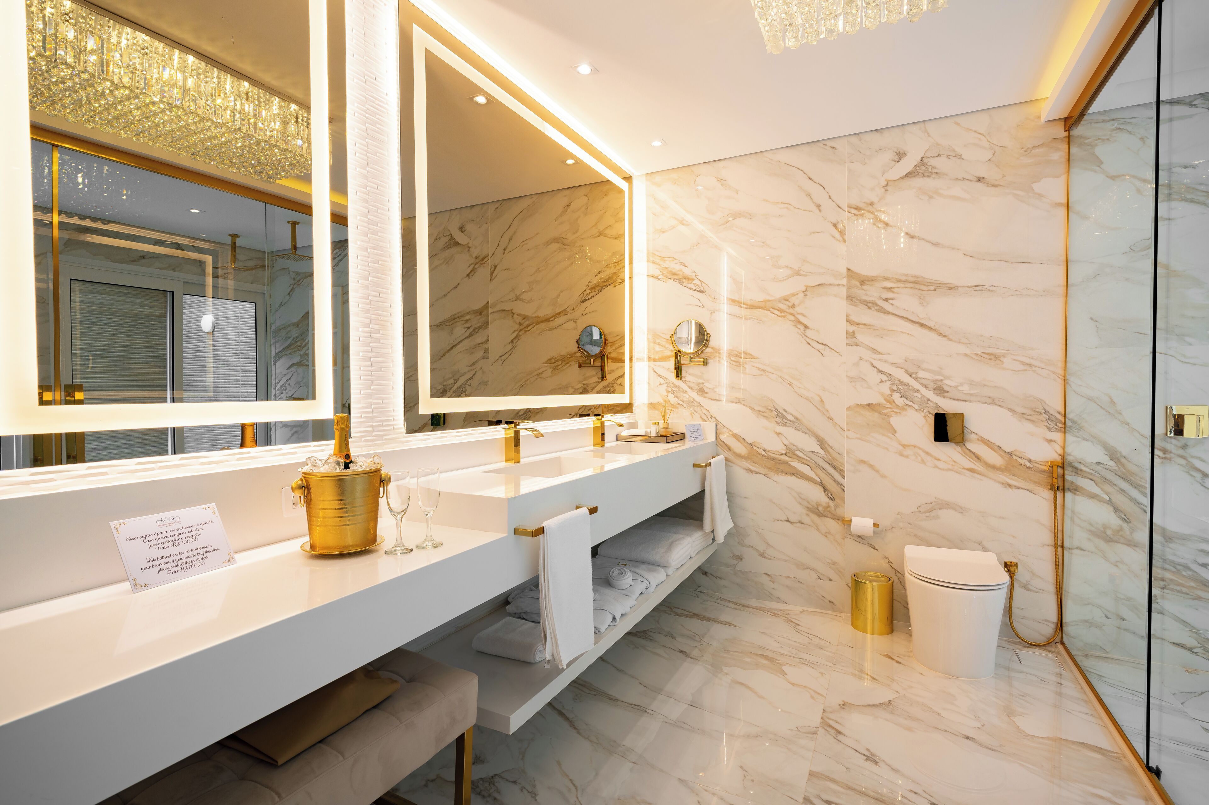 A modern bathroom with marble walls, a large mirror, dual sinks, and a shower area.