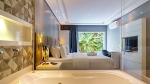 A modern bathroom with a large bathtub, a vanity with a mirror, and a window with a view of palm trees. - Pousada Apple House Paraty (Paraty)