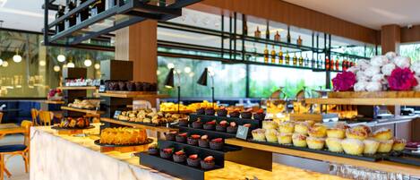 A bakery counter with various pastries and baked goods, shelves with bottles, and a seating area with chairs.