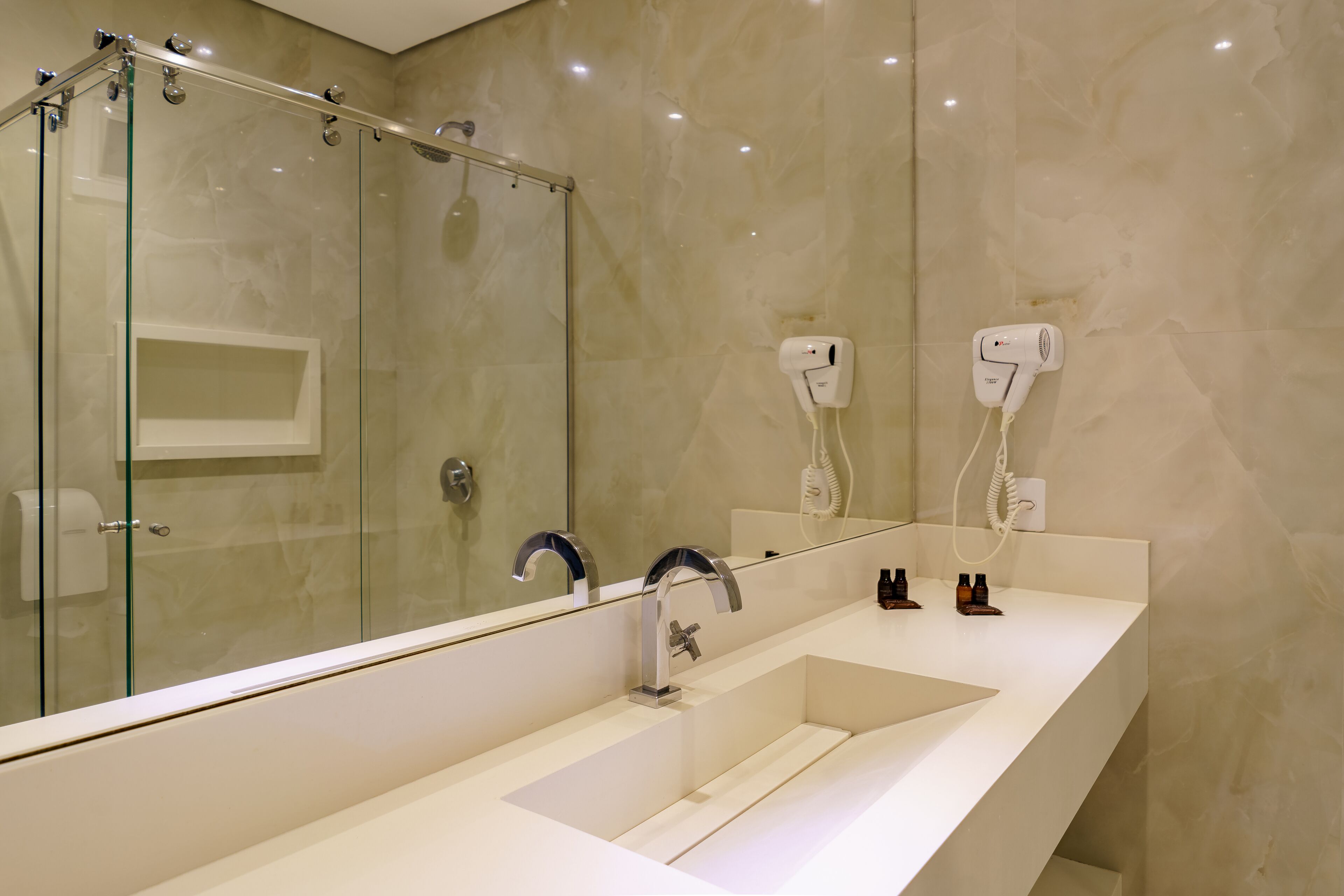 A modern bathroom with a glass-enclosed shower, a large mirror, and a white sink with two faucets.
