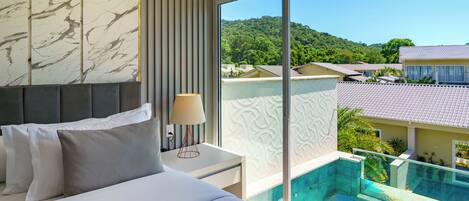 A bedroom with a bed, bedside table, lamp, and a view of a swimming pool and hillside.