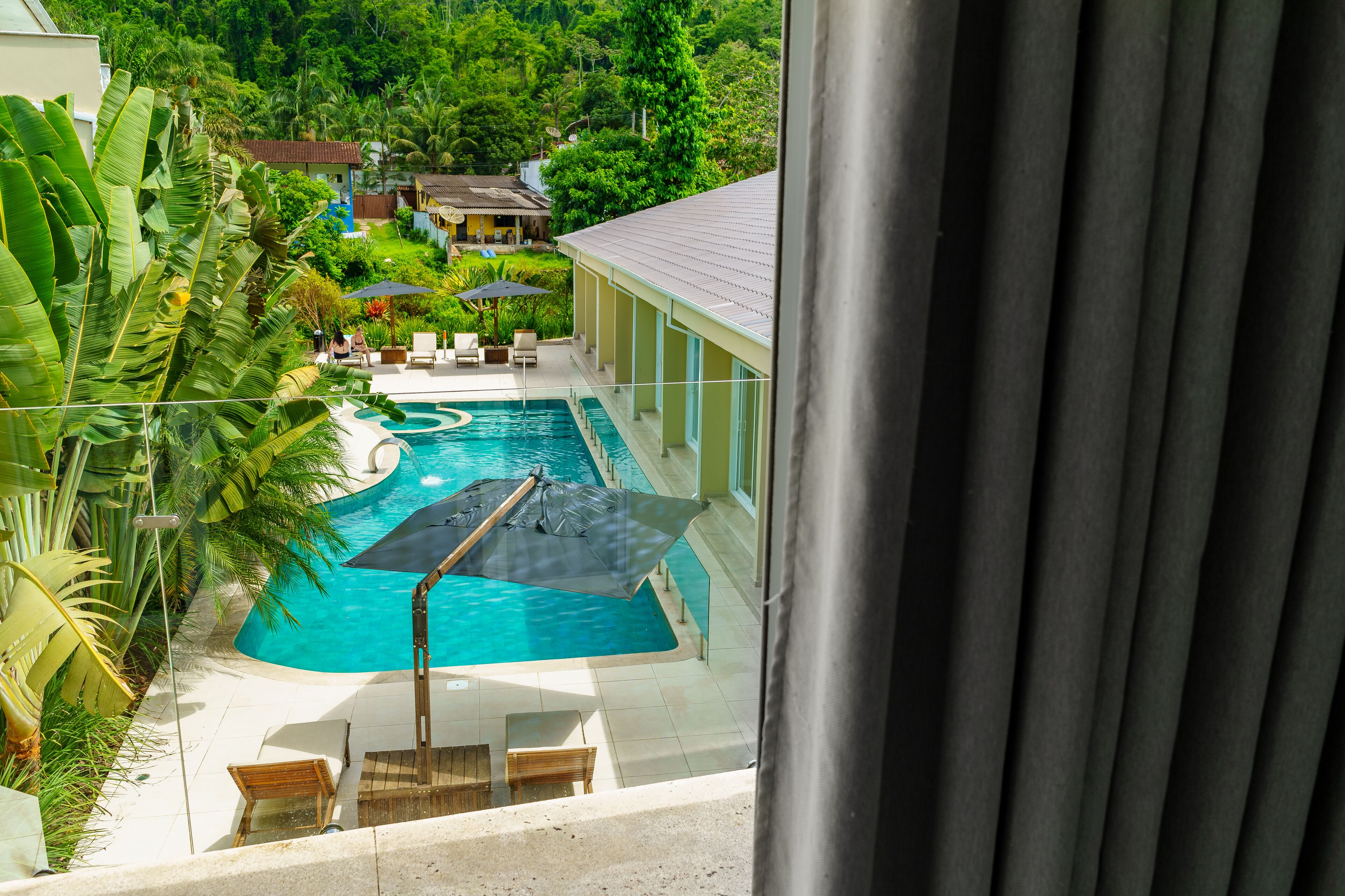 A swimming pool with lounge chairs and umbrellas, surrounded by lush greenery and a view of a residential area.