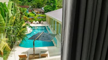 A swimming pool with lounge chairs and umbrellas, surrounded by lush greenery and a view of a residential area.