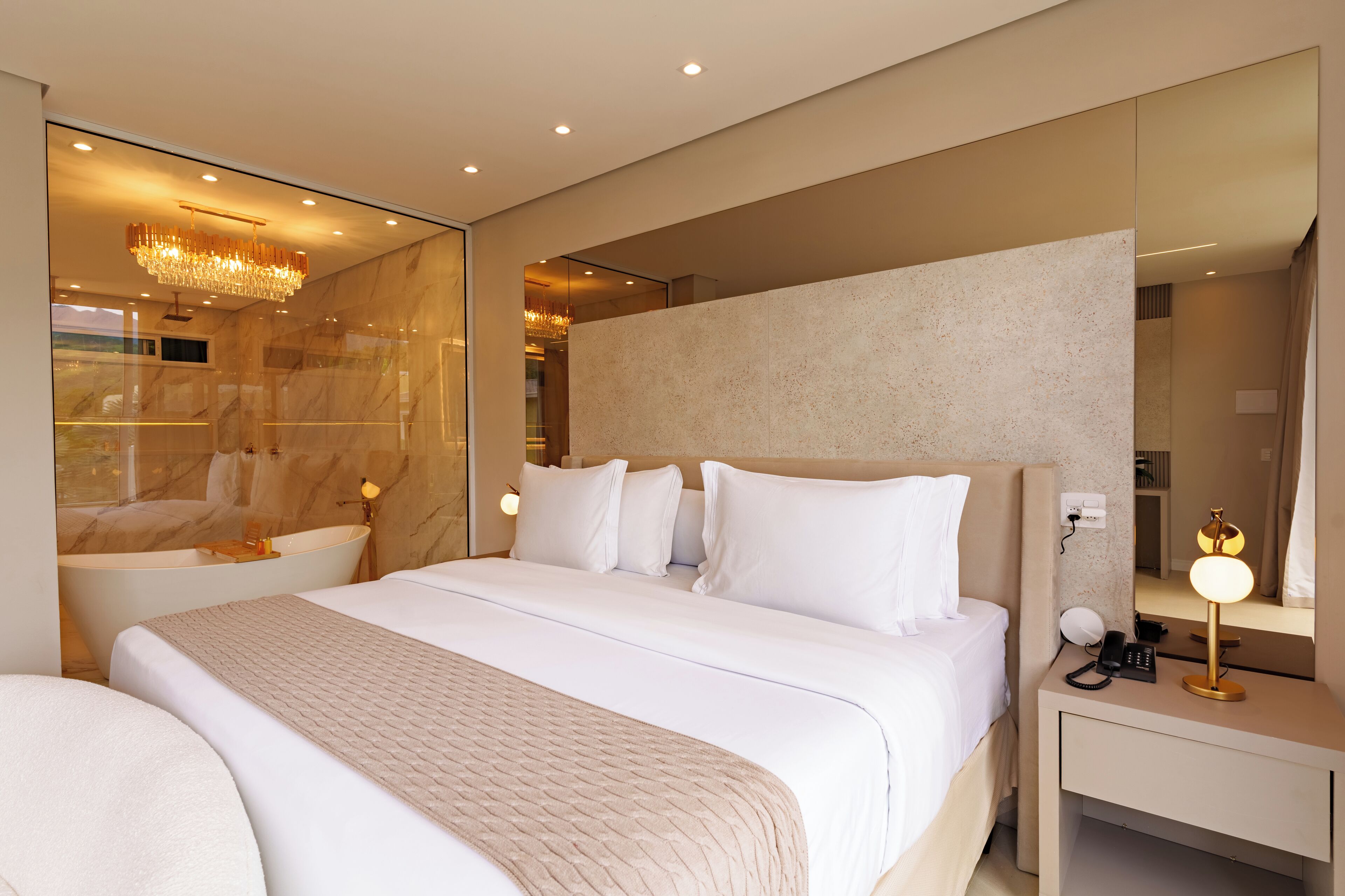 Una habitación de hotel moderna con una cama grande, una bañera integrada, una mesita de noche con lámpara y un espejo amplio.