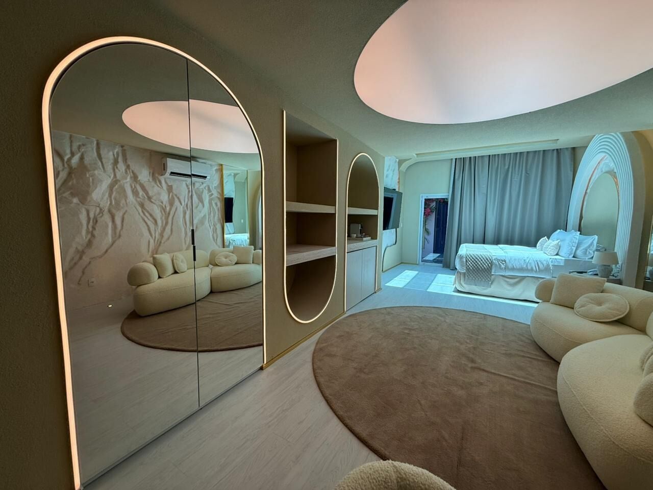 Une chambre d’hôtel moderne avec un grand miroir, un tapis rond, un canapé et un lit.