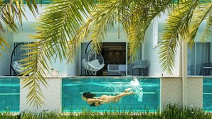 A swimming pool with a person swimming, surrounded by palm trees and a building with outdoor seating. - Pousada Apple House Paraty (Paraty)