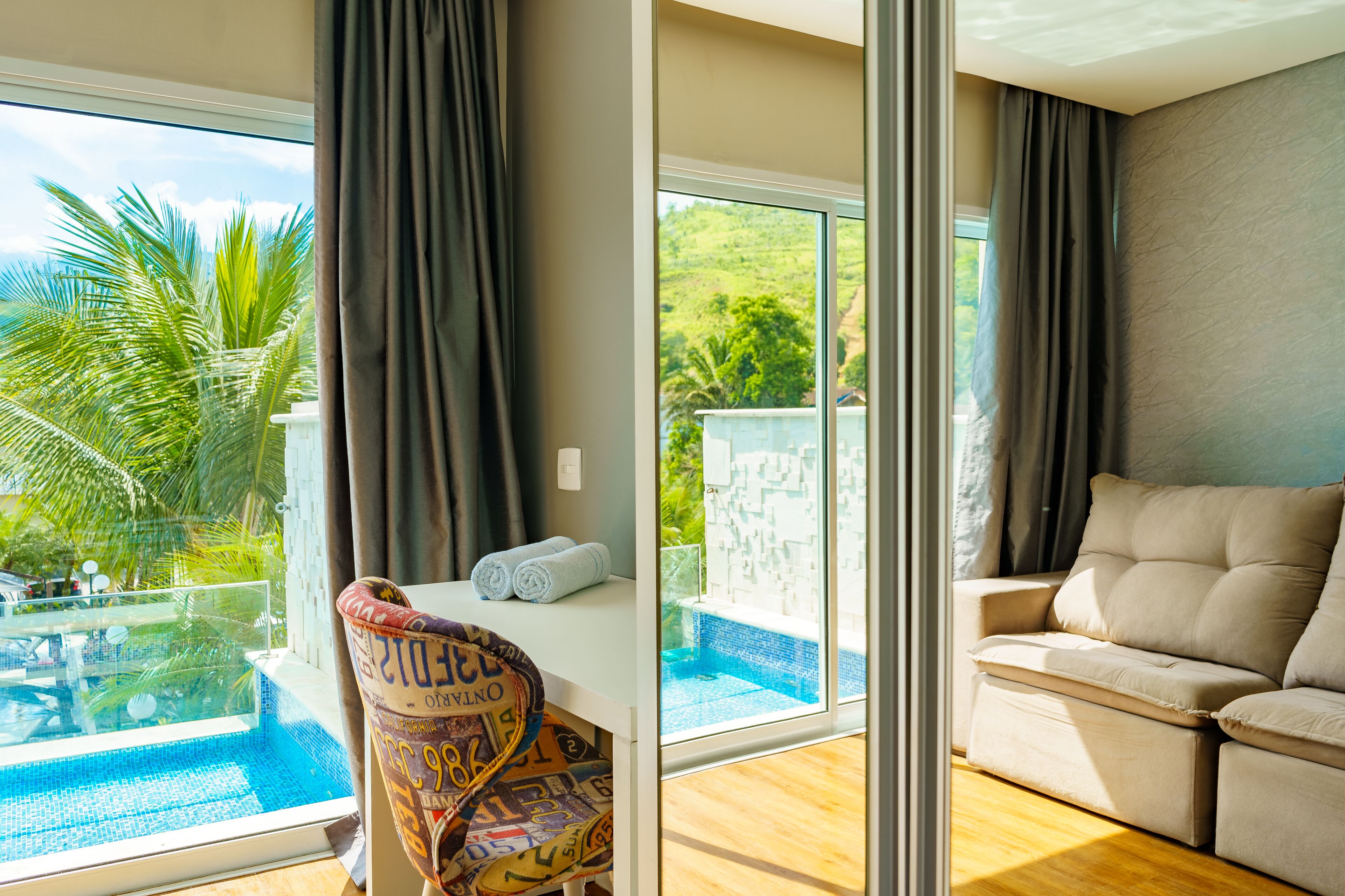A room with a view of a swimming pool, a sofa, and a chair with a patterned cushion.