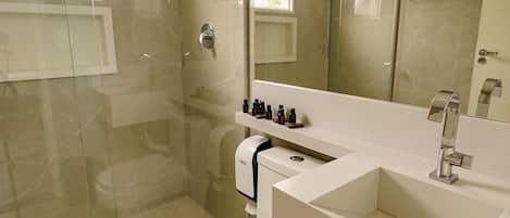 Un baño moderno con ducha de vidrio, lavamanos blanco y espejo sobre el tocador.