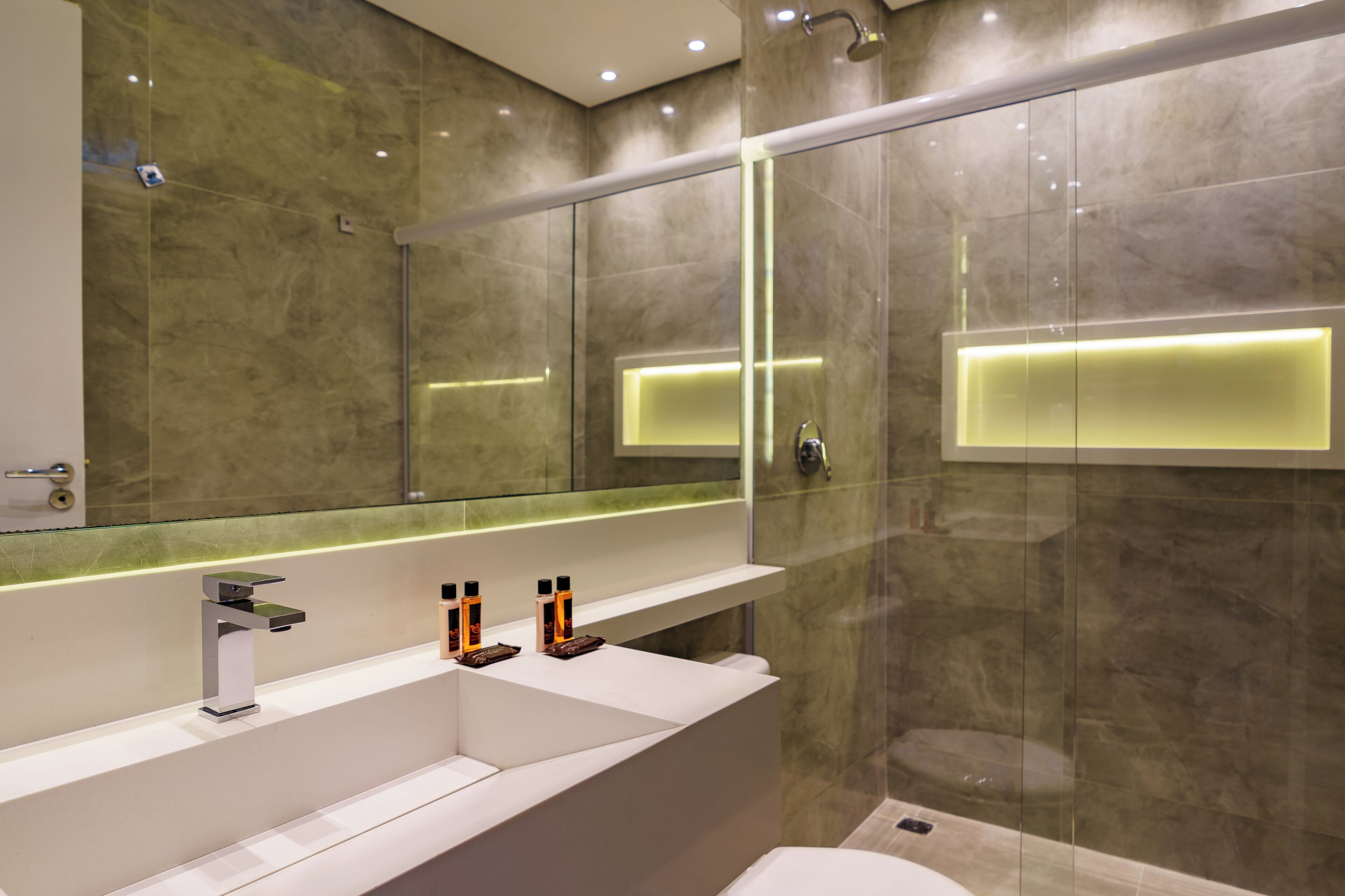 Un baño moderno con ducha de vidrio, tocador blanco con espejo y panel de luces empotradas.
