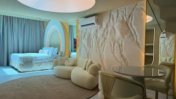 Een moderne hotelkamer met een bed, een ronde salontafel en een zithoek met banken.