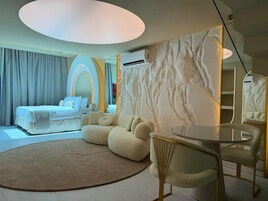 Een moderne hotelkamer met een bed, een ronde salontafel en een zithoek met banken.