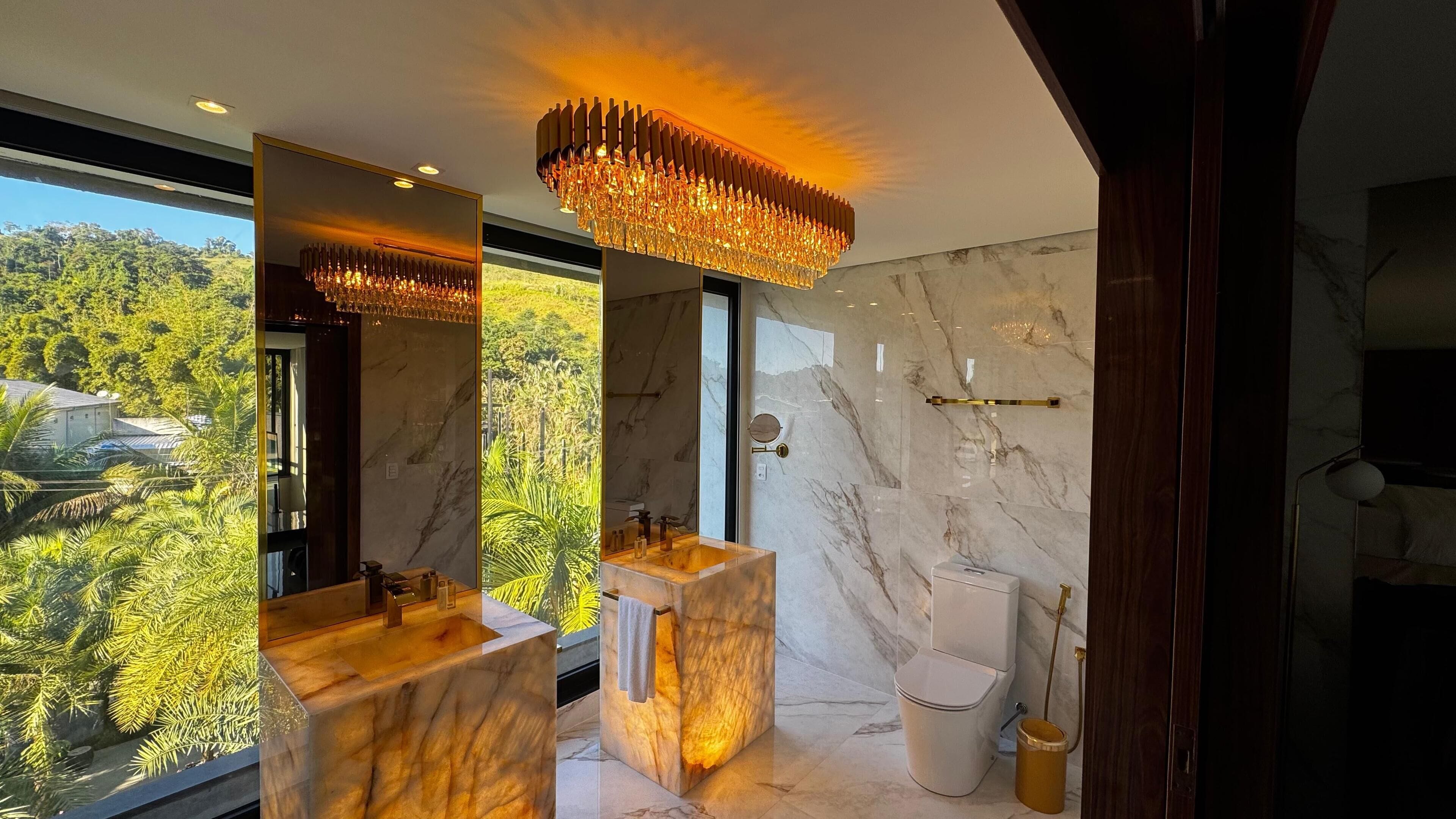 A modern bathroom with marble countertops, a large mirror, and a chandelier.