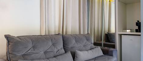 Un sofá gris con varios cojines, un armario blanco y un espejo que refleja la habitación.