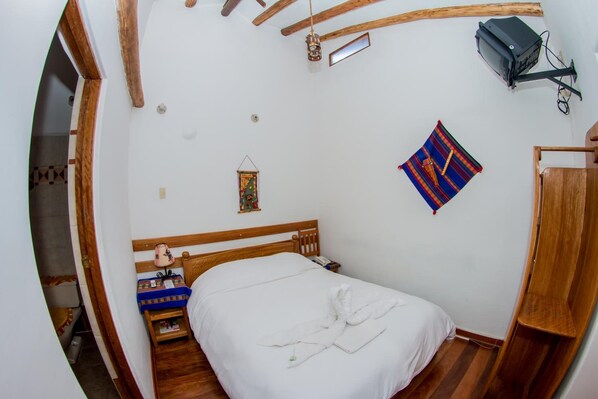 A compact hotel room with a wooden bed, a small bedside table, a wall-mounted projector, and a colorful tapestry. - Hostal El Grial (Cusco)