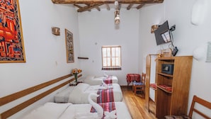 A hotel room with three beds, each with a swan-shaped pillow and a colorful blanket. There is a wooden desk with a television and a small table with a red tablecloth. - Hostal El Grial (Cusco)