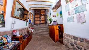 A narrow hallway with wooden benches, a wooden desk, and a large mirror on the left. - Hostal El Grial (Cusco)