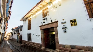 A narrow street with white buildings, a hostel sign, and a medical facility sign. - Hostal El Grial (Cusco)