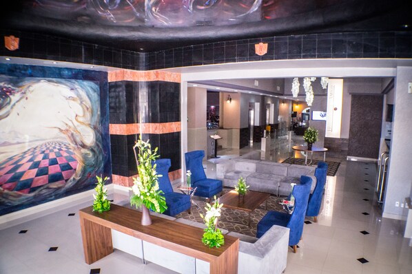 Un hall d’entrée moderne agrémenté d’une grande fresque murale abstraite, de sièges bleus, d’un comptoir d’accueil en bois et d’une cloison en verre donnant sur un espace d’accueil.