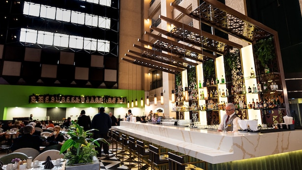 Zona de bar moderna con una barra larga, asientos y vistas a un edificio con amplios ventanales.