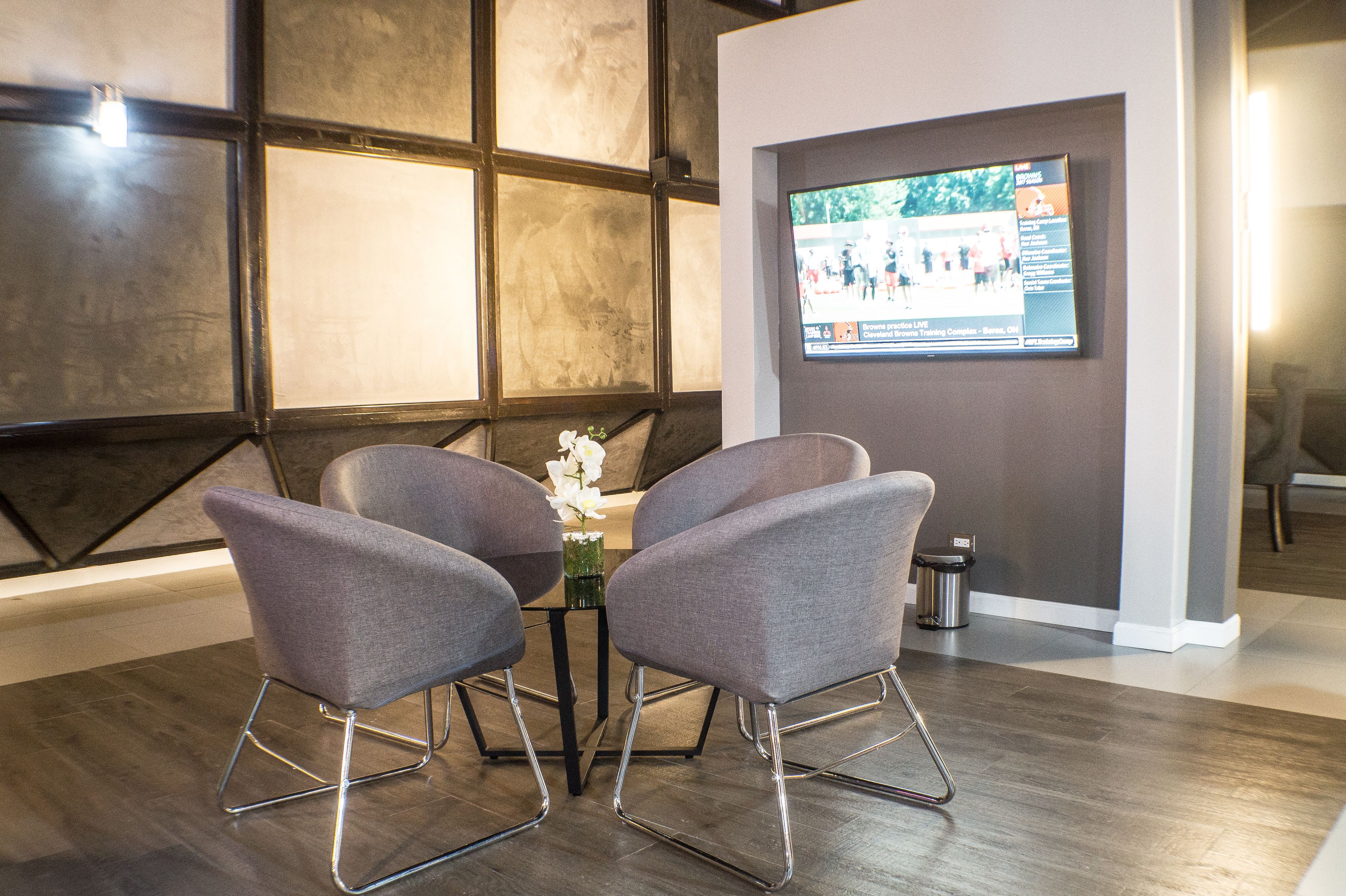 A conference room with a modern design, featuring a large screen for presentations, grey upholstered chairs, and a small table with a vase of flowers.