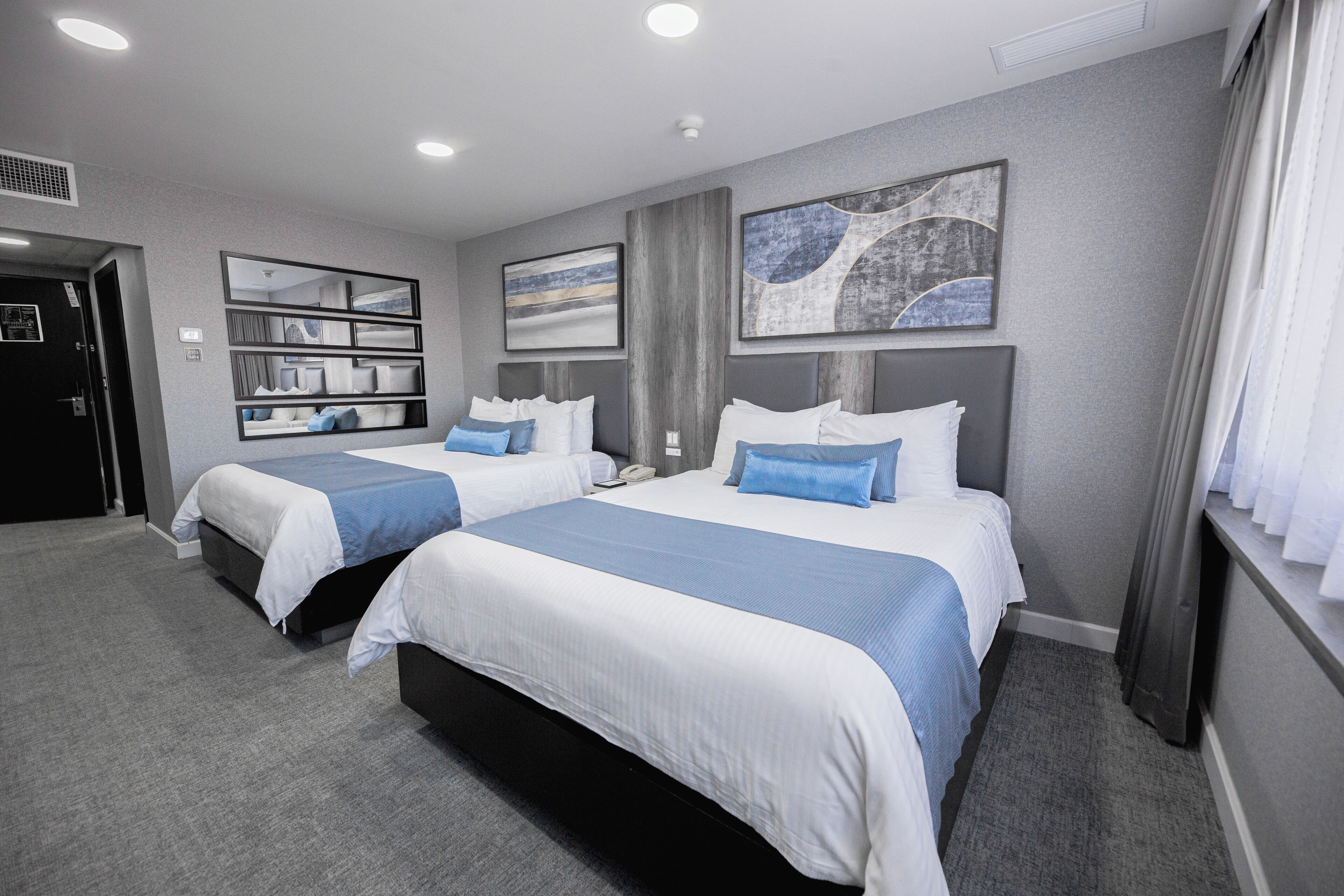 A hotel room with two beds, a large mirror, and artwork on the walls.