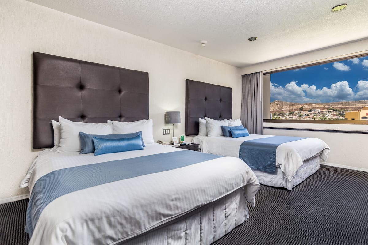 A hotel room with two beds, a large window with a city view, and a modern design.