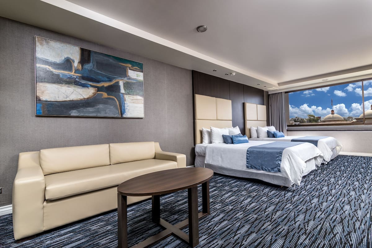 A hotel room with a large bed, a sofa, a small table, and a large abstract painting on the wall.