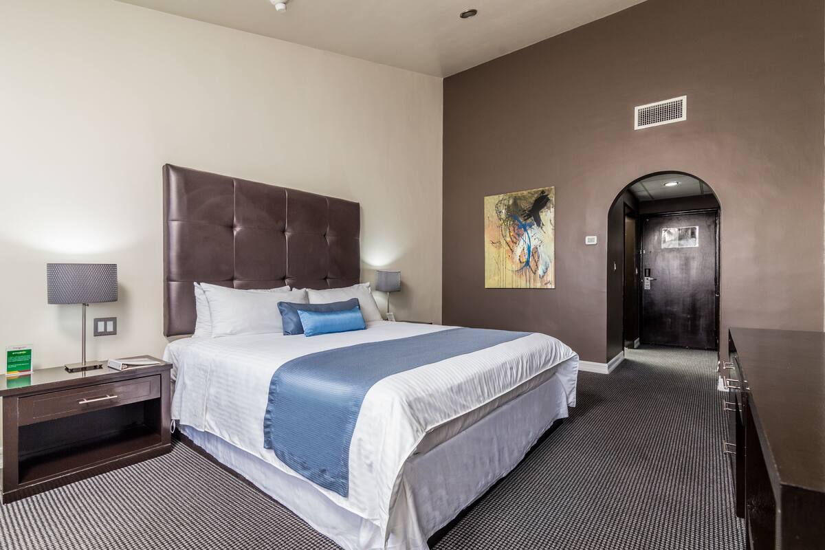A hotel room with a large bed, a nightstand, a desk, a lamp, and a painting on the wall.